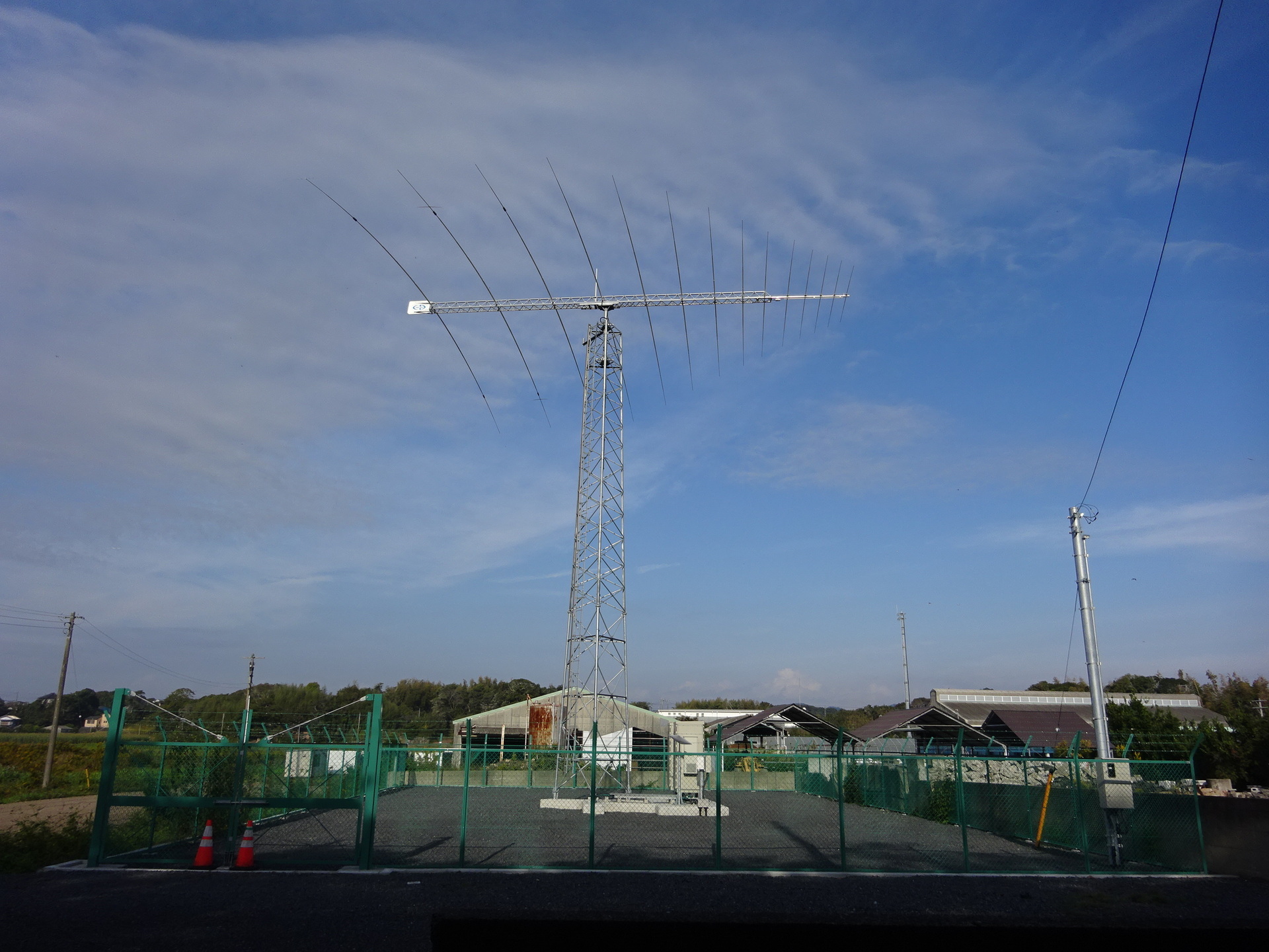 Minamihara’s receive installation: one fourteen-element log-periodic on a dedicated mast, with equipment cabinets inside the compound.